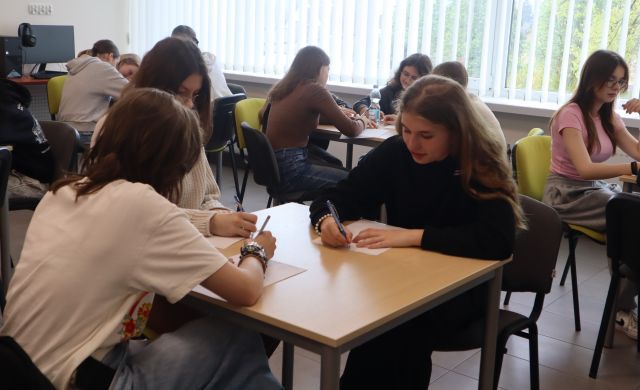 młodzież siedzi przy stolikach i pisze na kartkach