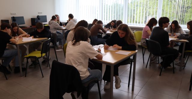 młodzież siedzi przy stolikach i pisze na kartkach