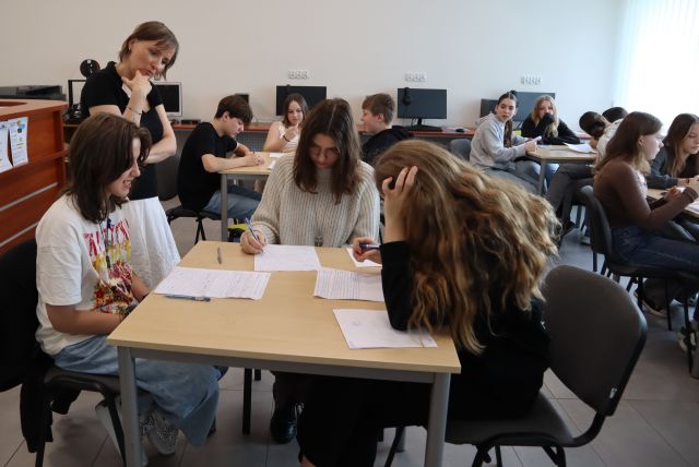 młodzież siedzi przy stolikach i pisze na kartkach