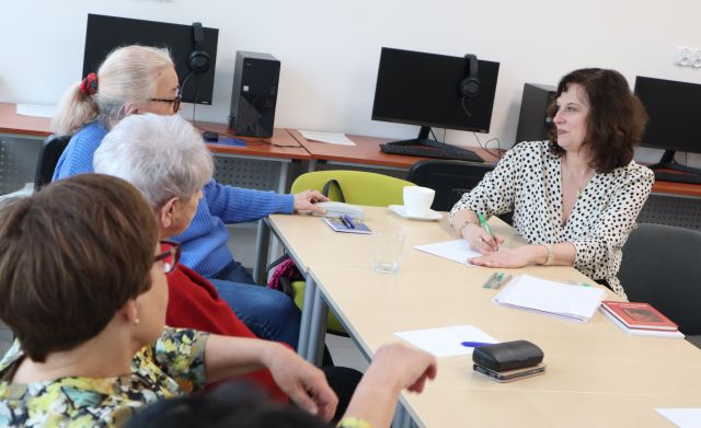 przy stolikach siedzą seniorki i kobieta, która pisze na kartce