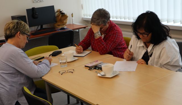 seniorki siedzą przy stołach i piszą na kartkach