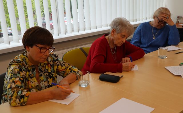 seniorki siedzą przy stołach i piszą na kartkach