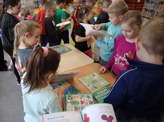 przedszkolaki przy stołach przeglądają książki