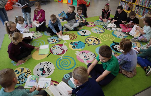 przedszkolaki siedzą na kolorowym dywanie i przeglądają książki