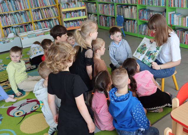 dzieci stoją przed siedzącą bibliotekarka z książką