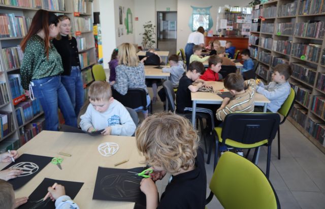 przedszkolaki siedzą przy stolikach, w tle regały z książkami