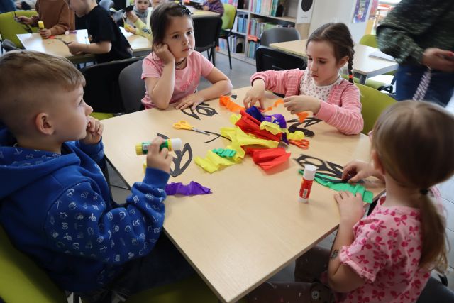przedszkolaki przy stolikach tną nożyczkami, w tle regały z książkami