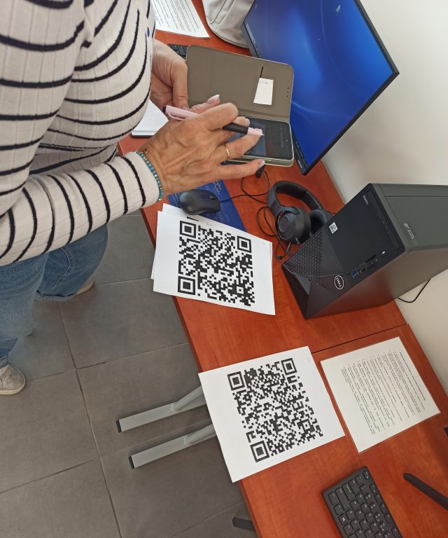 seniorka z telefonem, obok na stole leży kod QR