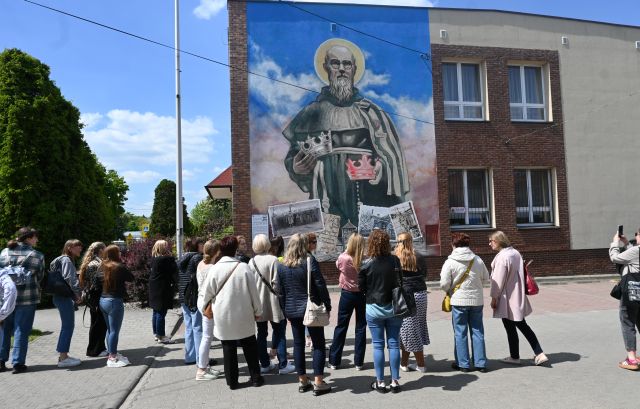 grupa osób stoi przed muralem z księdzem Maksymilianem Kolbe