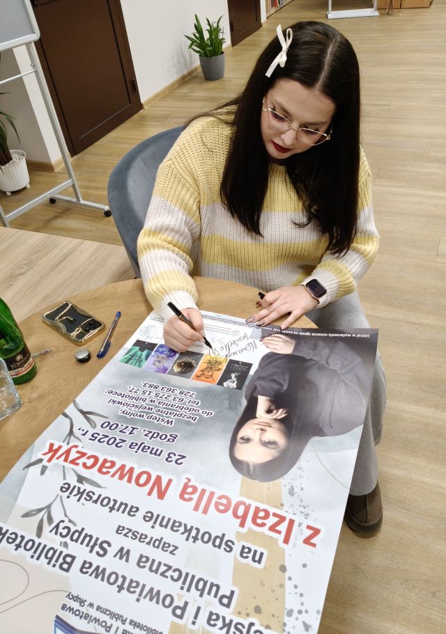 autorka podpisuje się na plakacie zapraszającym na spotkanie