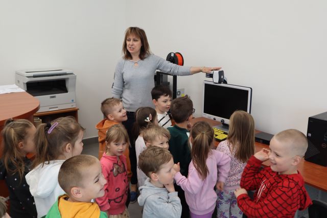 przedszkolaki i dyrektorka biblioteki stoją przed komputerem z lupą