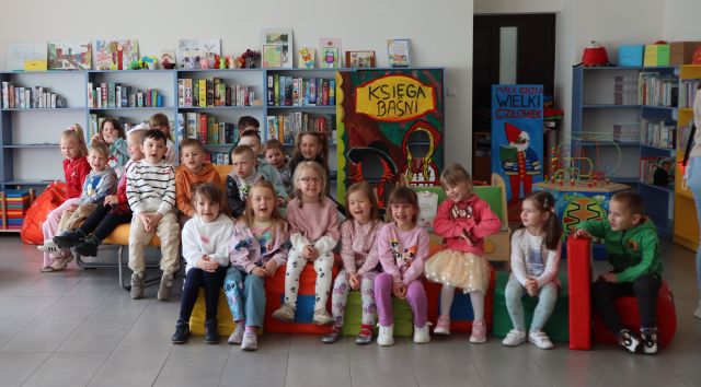 przedszkolaki siedzą na okrągłym siedzisku, w tle regały