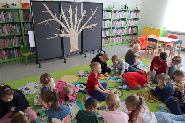 dzieci siedzą na kolorowym dywanie i rysują na kartkach