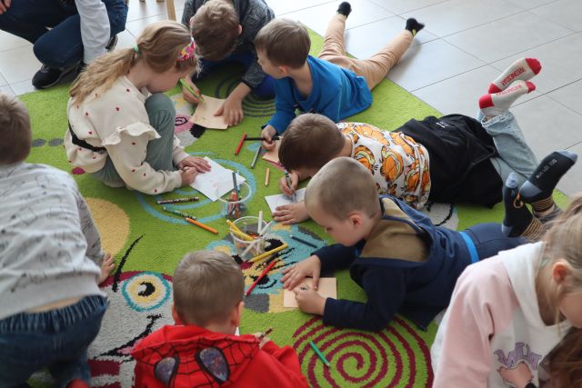 dzieci siedzą i leżą na kolorowym dywanie i malują na kartkach
