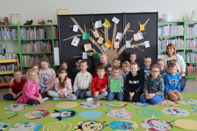 dzieci pozują do zdjęcia na tle drzewa z papieru naklejonego na tablicę, na drzewie pouczepiane kartki