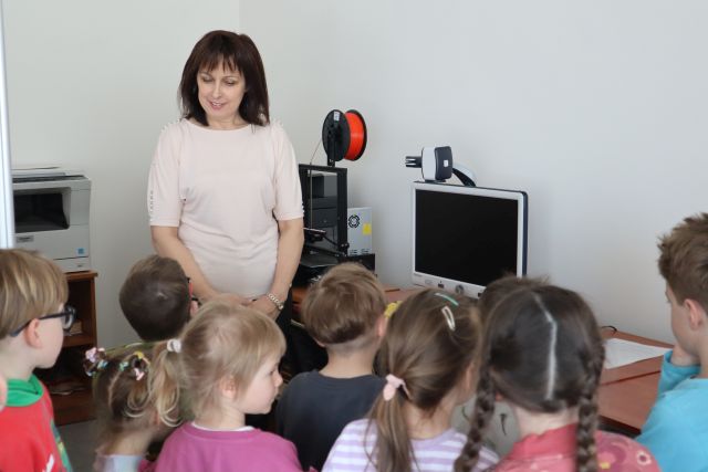 dzieci stoją przed dyrektorką biblioteki w sali komputerowej