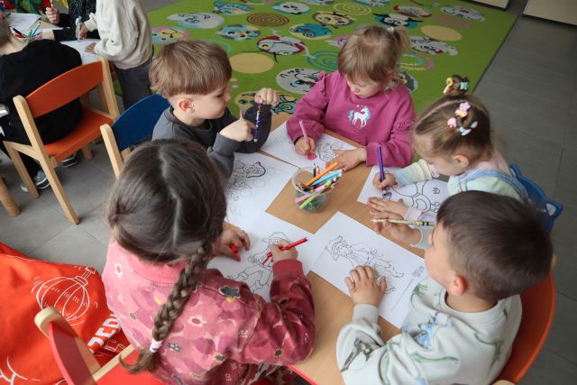 przedszkolaki siedzą przy stoliku i kolorują rysunki