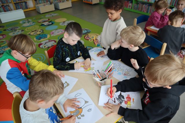 przedszkolaki siedzą przy stoliku i kolorują ilustracje
