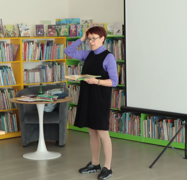 kobieta z książką, i podniesioną do głowy ręką, w tle regały z książkami