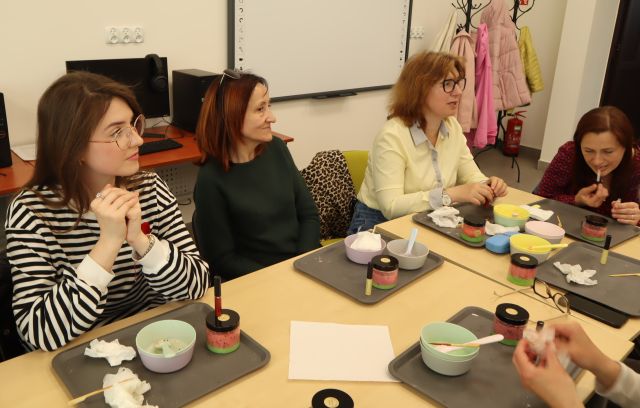 kobiety siedzą przy stołach, przed nimi zrobione przez nie kosmetyki