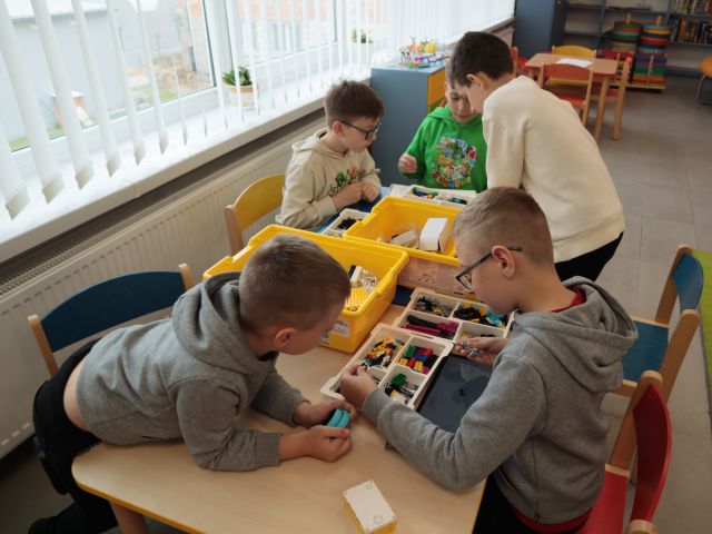 5 chłopców siedzi przy stolikach, przed nimi klocki Lego w pudełkach