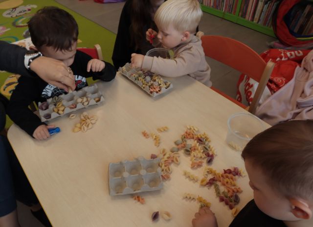 dzieci i mamy przekłądają kolorowy makaron po pudełęk po jajkach