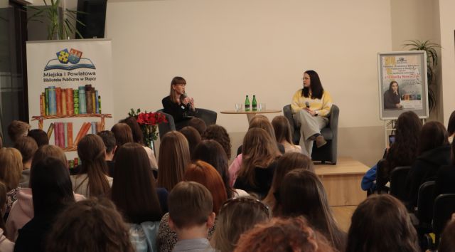 dwie młode dziwczyny siedzą na fotelach na scenie, przed nimi siedzi tłum młodych osó uczestniczących w spotkaniu