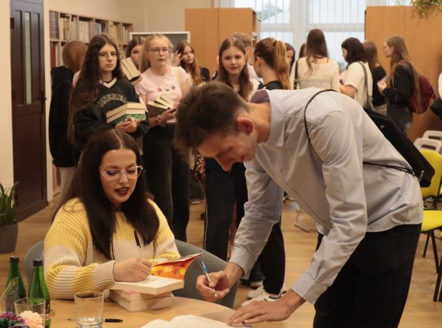 dziewczyna podpisuje chłopakowi książki, w tle kolejka czekających młodych osób