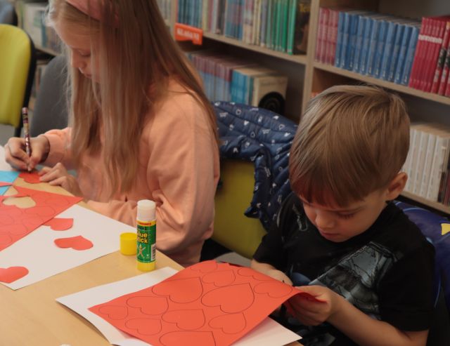 chłopiec i dziewczynka wycinają z kartek serduszka