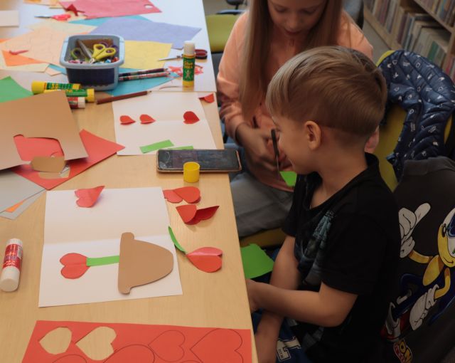 dziewczynka i chłopiec naklejają na kartkę serduszka