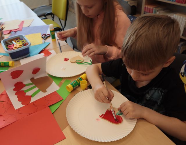 dziewczynka i chłopiec malują na czerwono drewniane serduszka