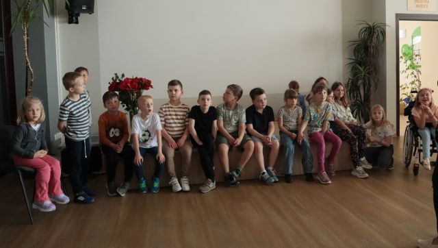 dzieci siedzą na scenie w holu biblioteki