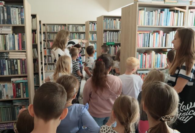 dzieci i bibliotekarka między regałami z książkami