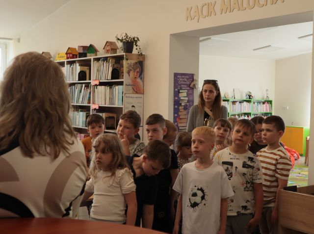dzieci stoją przed bibliotekarką, w tle regały z książkami