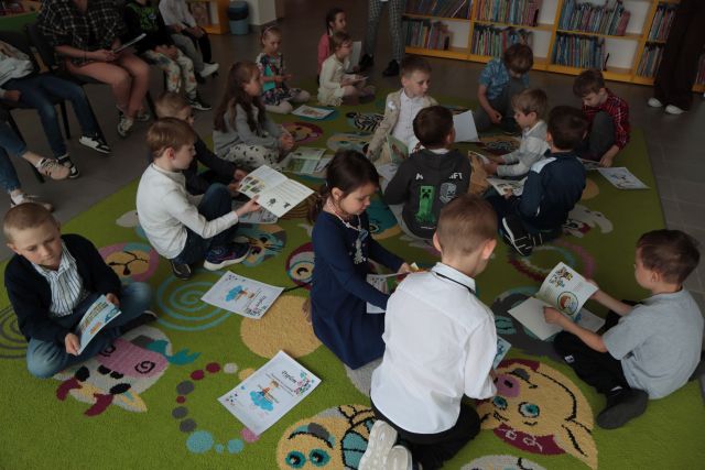 dzieci siedzą na dywanie i przeglądają książki i dyplomy