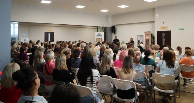 uczestnicy spotkania siedzą na krzesłach, w tle prowadzący i autorka