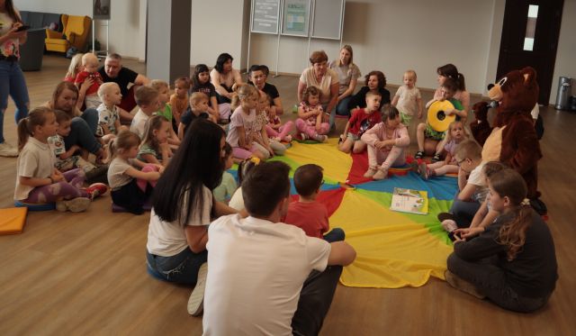 miś czyta dzieciom siedzącym na chuście animacyjnej