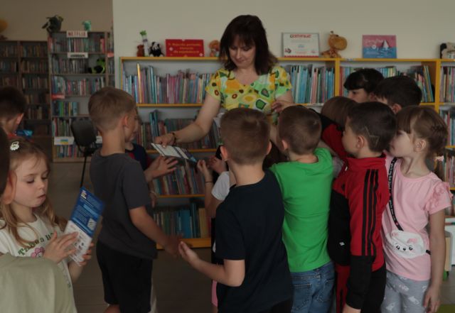 dyrektorka biblioteki rozdaje dzieciom kaledarzyki, w tle regały z książkami