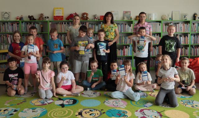 dzieci z bibliotekarką, dyrektorką biblioteki i nauczycielką pozują do zdjęcia na tle regałów z książkami