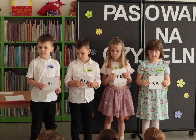 4 dzieci stoi z kartkami tworzącymi hasło Biblioteka