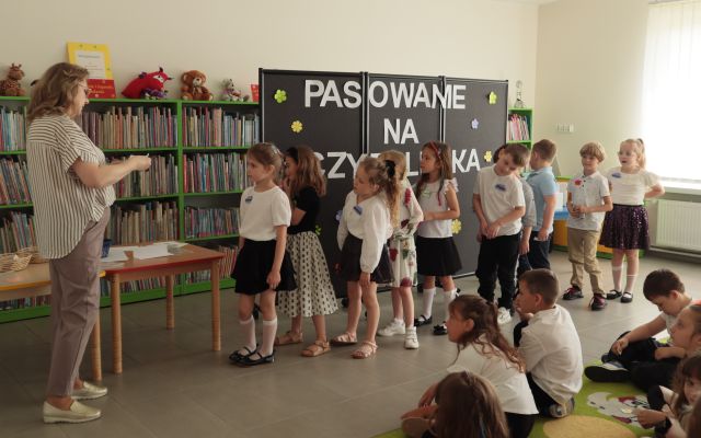dzieci stoją przed bibliotekarką z kartkami