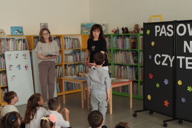 dyrektorka biblioteki pasuje chłopca ogromnym ołówkiem na czytelnika biblioteki