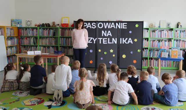 dyrektorka biblioteki stoi przed siedzącymi na dywanie przedszkolakami