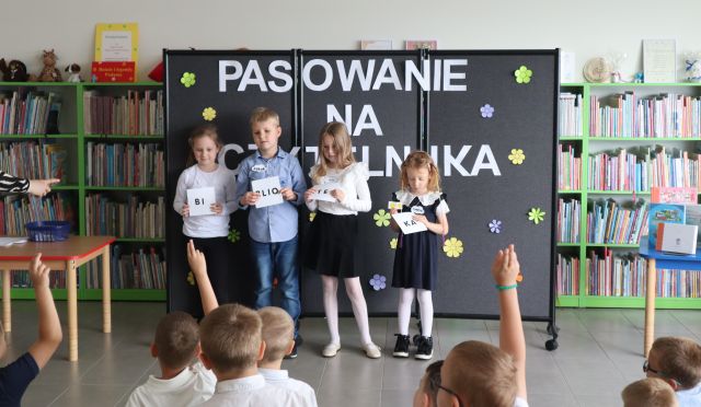 4 dzieci stoi z karteczkami z hasłęm Biblioteka