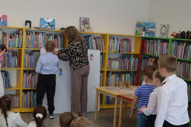 chłopiec z bibliotekarką przypinają do tablicy ilustracje postaci bajkowych