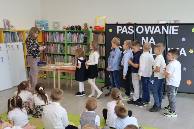 na zdjęciu dzieci stoją w rzędzie przed bibliotekarką