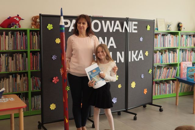 na zdjęciu dziewczynka z książką i dyrektorka biblioteki z ogromnym ołówkiem