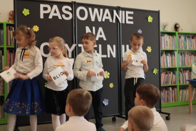 4 dzieci stoi z kartonikami z hasłęm biblioteka
