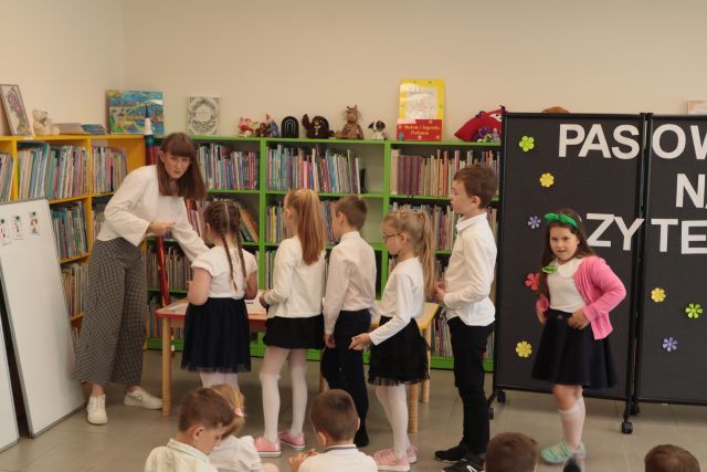 dzieci stoją w rzędzie przed bibliotekarką