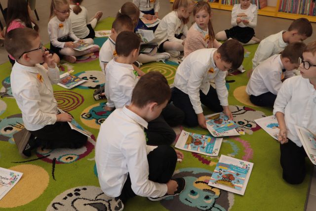 przedszkolaki siedzą na dywanie i przeglądają książki